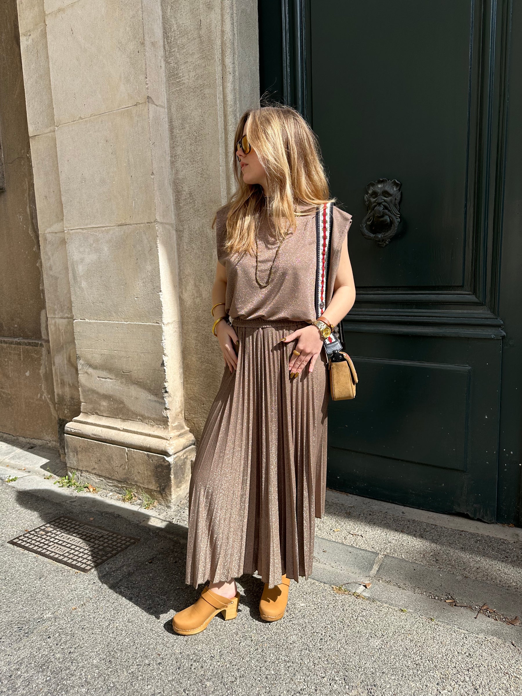 Vue d'ensemble de la jupe longue à paillettes Momoni de chez Charlotte Avignon portée sur une femme blonde devant une porte verte.